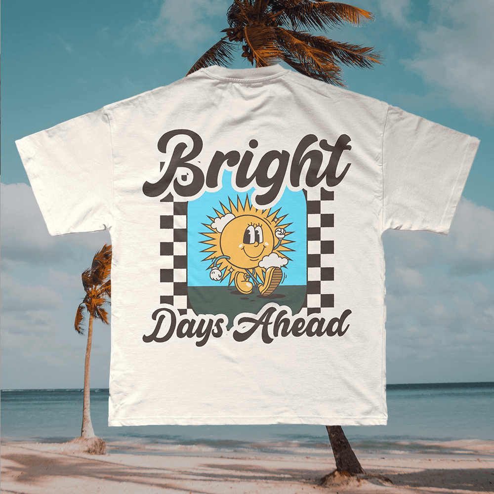 A merch mockup of a cream tee on a beach, printed Bright Days Ahead in brown retro script around a cartoon sun in sneakers on a checkerboard frame.