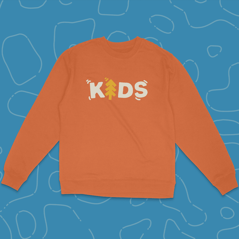 An orange crewneck sweatshirt on a blue squiggle background, printed KIDS in chunky cream lettering with a yellow pine tree replacing the I.