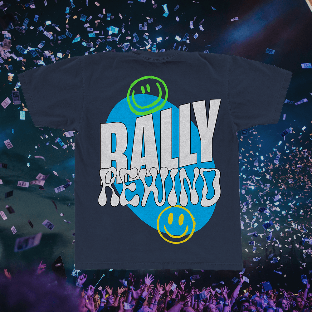 A merch mockup of a navy tee over a confetti filled arena, printed RALLY REWIND in white block and bubble type on a blue blob, with green and yellow smiley faces.