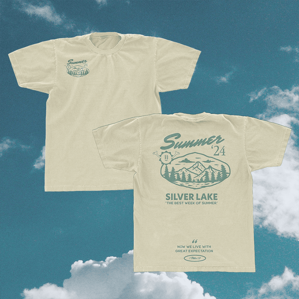 A merch mockup of two sand coloured tees against clouds, printed Summer '24 SILVER LAKE in green with a mountain badge and THE BEST WEEK OF SUMMER.