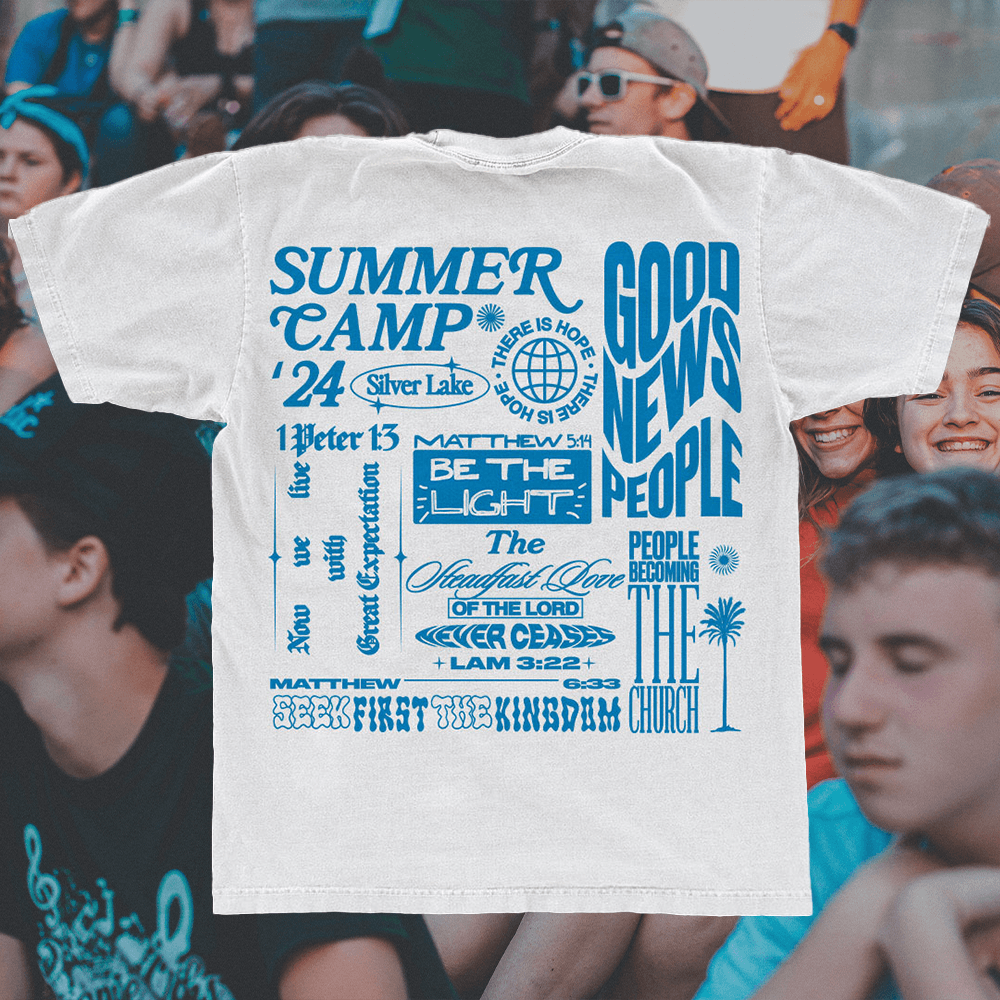 A merch mockup of a cream tee worn in a crowd, printed SUMMER CAMP '24 Silver Lake in blue with GOOD NEWS PEOPLE, BE THE LIGHT and Matthew and Lamentations verses.