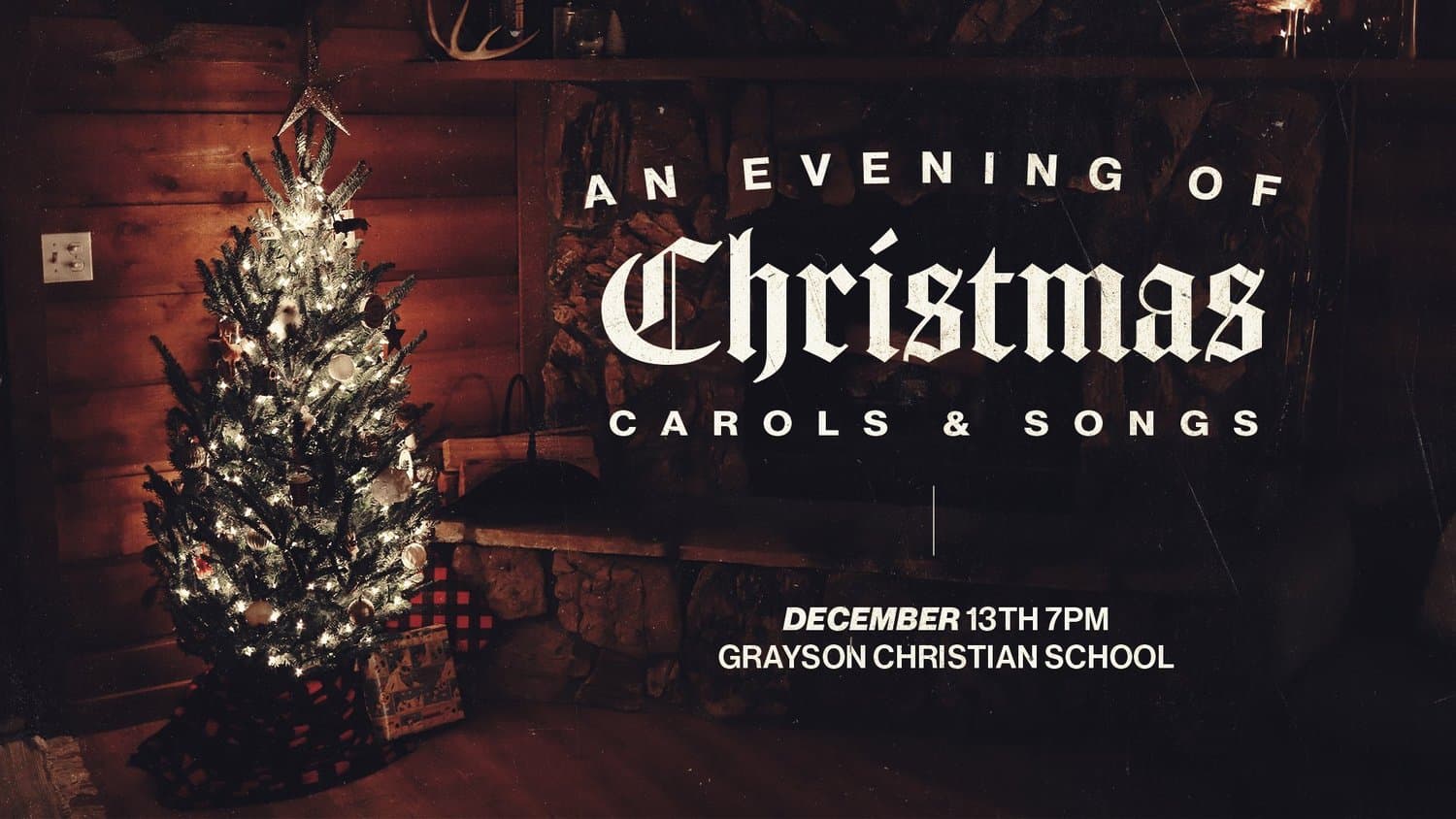 A Christmas concert slide reading AN EVENING OF Christmas CAROLS AND SONGS in blackletter and cream capitals, over a dim photo of a lit tree in a wood panelled room.