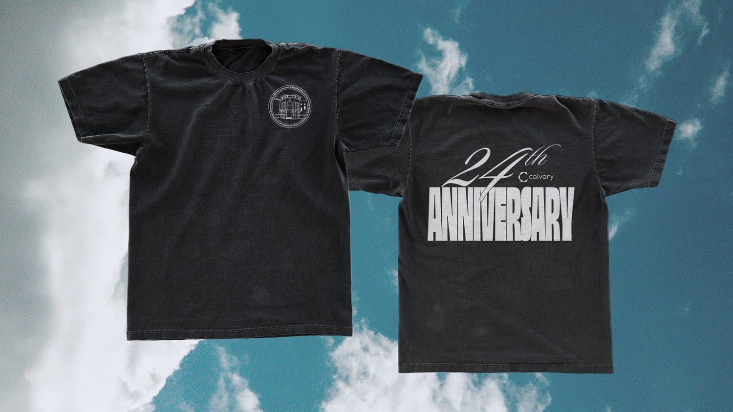 A merch mockup of two washed black tees against a cloudy sky, with a circular building crest on the chest and 24th ANNIVERSARY in script and chrome capitals on the back.