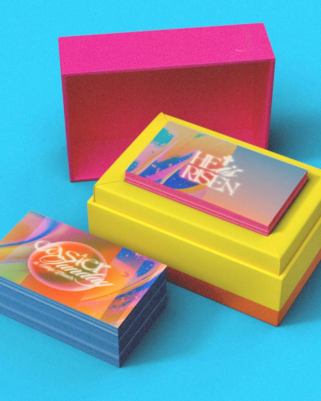 An invite card mockup on bright blue, two stacks of gradient cards reading HE is RISEN and easter sunday in glowing type, resting on pink and yellow boxes.