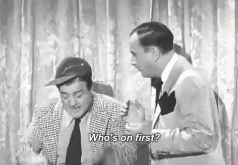 A black and white Abbott and Costello clip captioned Who's on first?, with one man in a flat cap shrugging while the other gestures at him in front of a stage curtain.