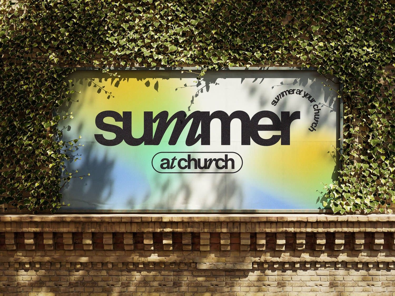 An outdoor billboard mockup on an ivy covered brick wall, printed summer in heavy black lowercase over a blue, yellow and green gradient, with at church in a pill outline beneath.